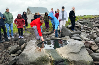 Hópur fólks virðir fyrir sér litla laug í stórum steini. Að baki er grár himinn.