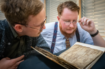 Two men with glasses look closely at an old manuscript.