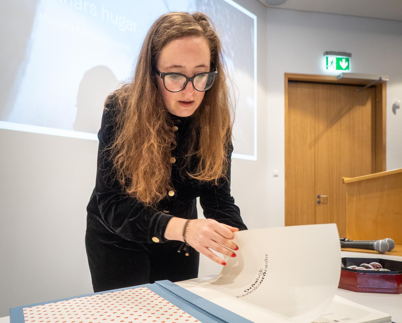 Kona flettir bók við borð í fyrirlestrasal. nærmynd.
