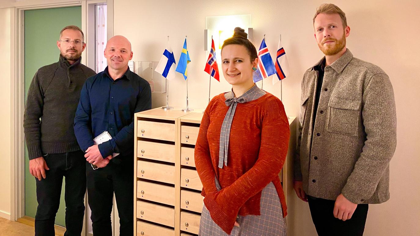 Þrír karlar og ein kona standa við kommóðu sem á eru fánar Norðurlanda