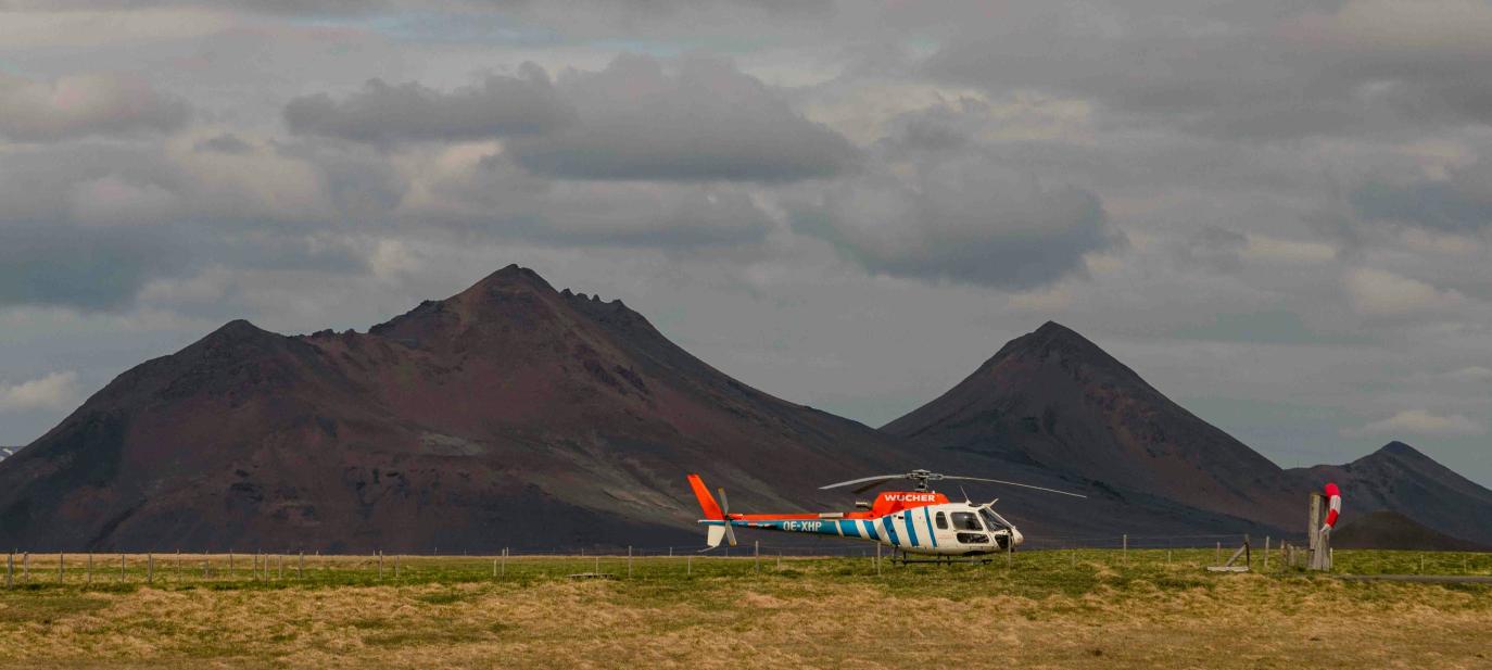 Þyrla á grasi, fjöll og grár himinn í baksýn.
