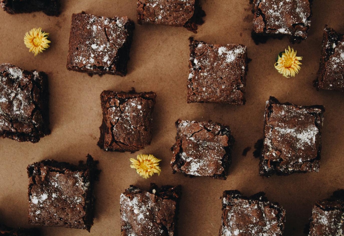 Horft ofan á ferkantaða brúnkubita (brownies). Inn á milli þeirra eru þrír gulir fíflar.