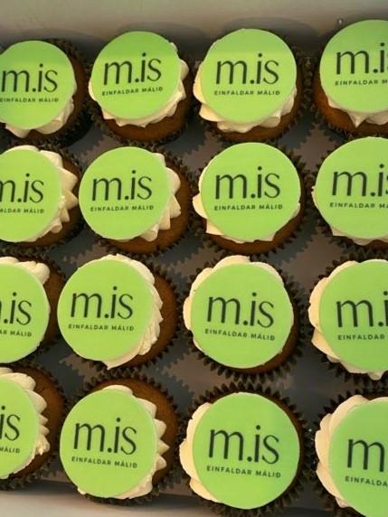 Cupcakes with a green disk balanced on top of white frosting. On the disk are the words "m.is: einfaldar málið", or "m.is: simplifies matters/language".