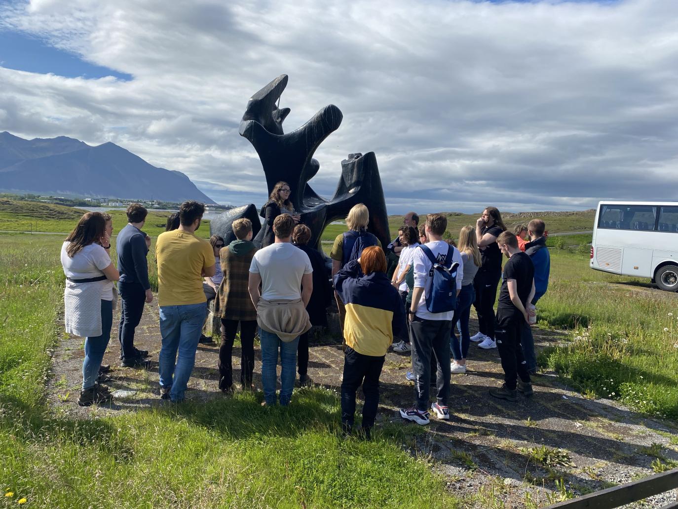 Hópur fólks virðir fyrir sér skúlptúr. Til hliðar glittir í rútu.