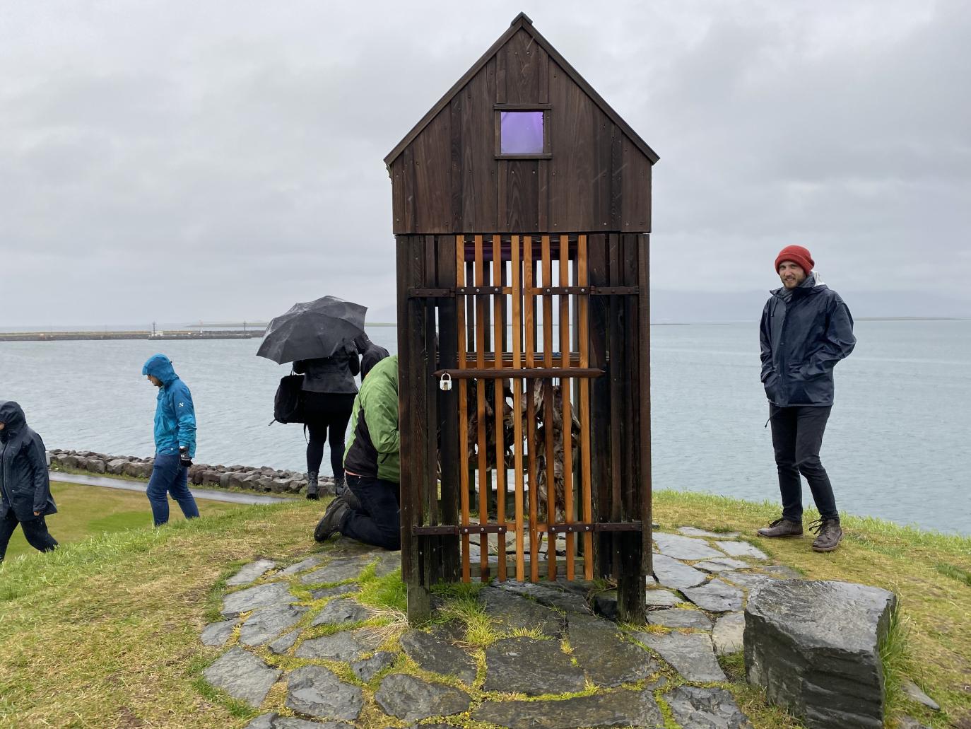 Fólk vappar í kringum örlítinn timburhjalla. Rigningarveður.