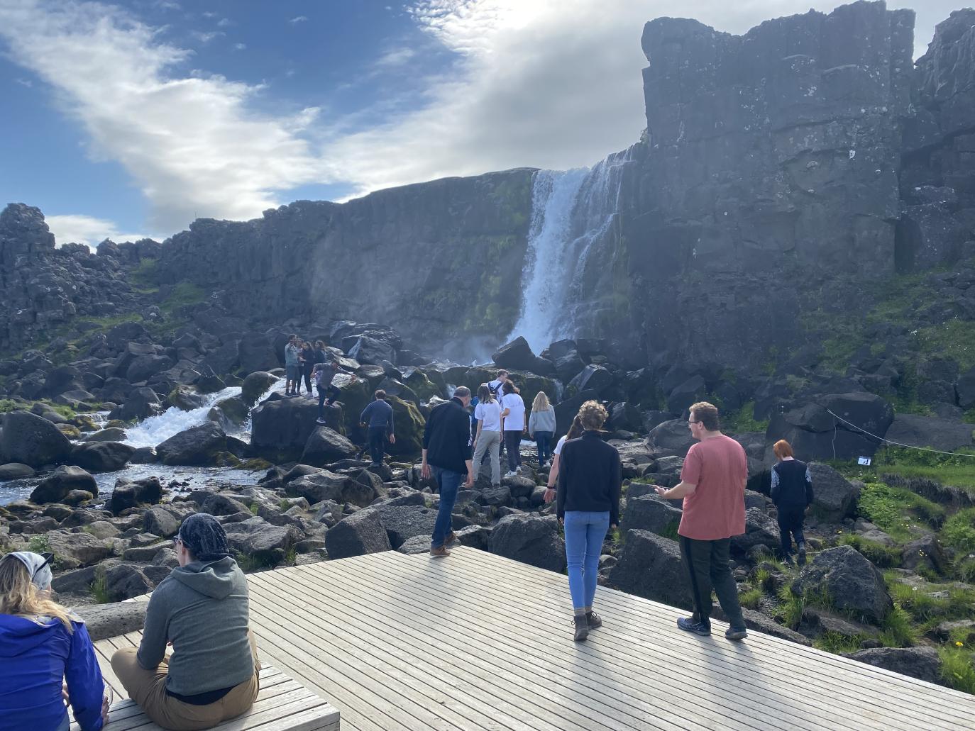 Hópur fólks á timburpalli virða fyrir sér kletta og foss.