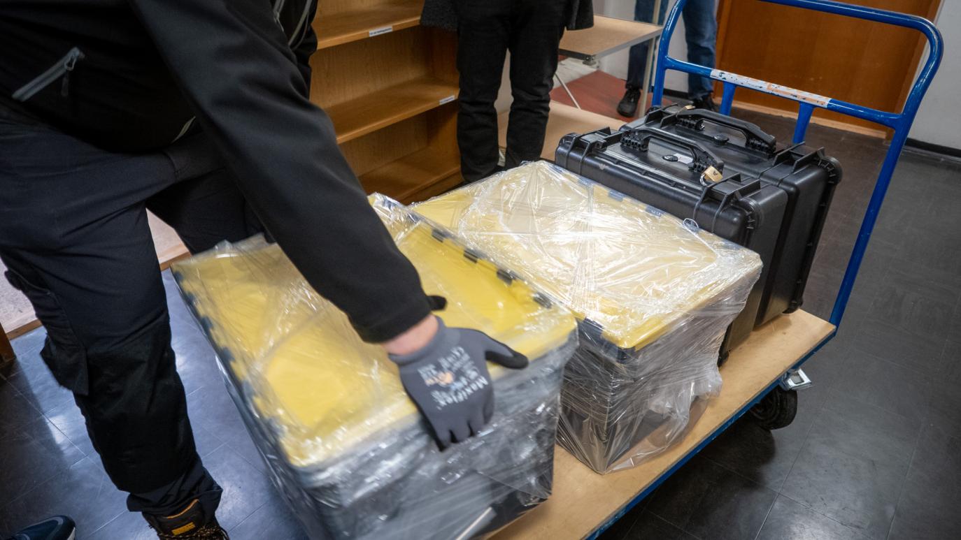 A person wearing gloves puts boxes wrapped in plastic on a cart.