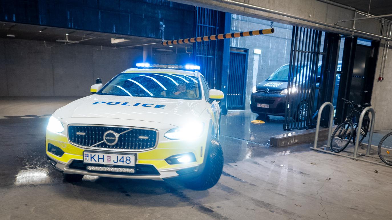 A police car drives into a parking garage. A black van follows.