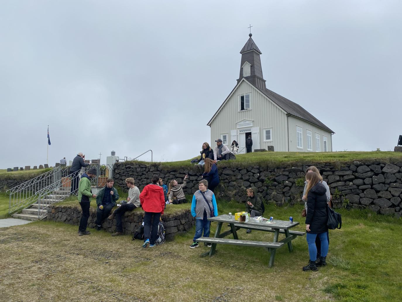 Hópur fólks fyrir framan hlaðinn vegg og kirkju.