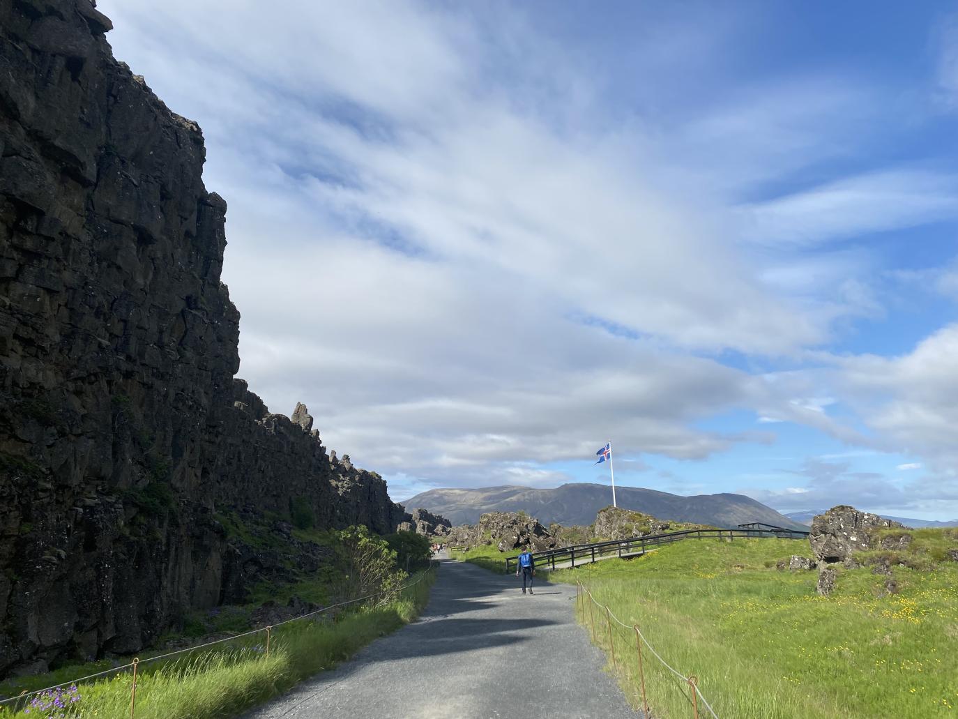 Göngustígur liggur meðfram háum kletti. Íslenskur fáni blaktir við hún.